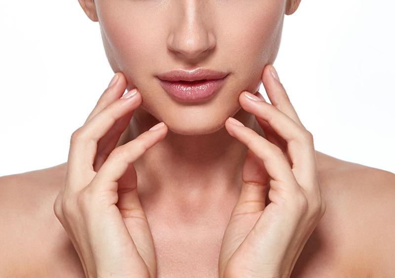 Close-up of a woman's lower face and jawline, with hands on either side of her chin, highlighting the balanced facial profile achieved through genioplasty by Dr. Steven R. Cohen at FACES+ in San Diego.